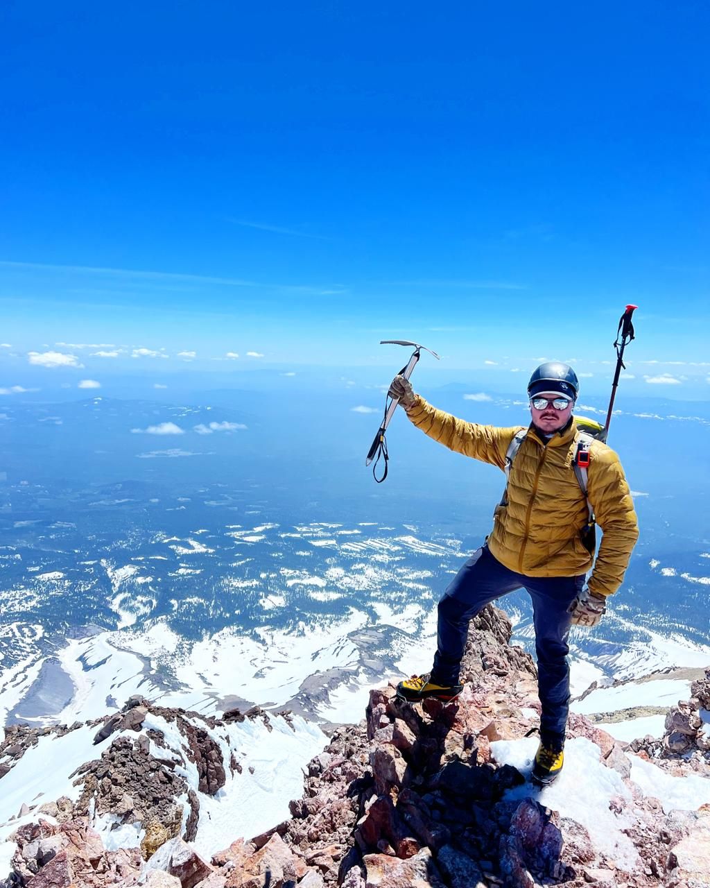 Trenton on the summit of Mount Shasta holding up an ice axe above the clouds